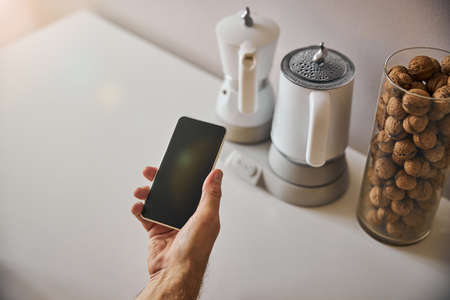 Person with a smartphone in hand in the kitchenの写真素材