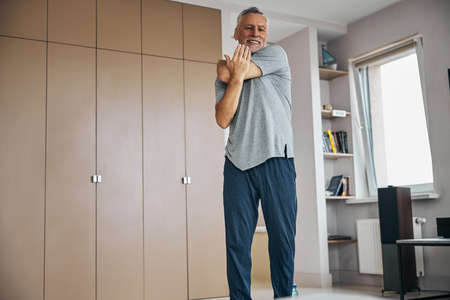 Aged man pressing on his elbow to stretch his arm
