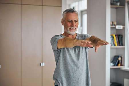 Gladsome aged man exercising at home and stretchingの写真素材