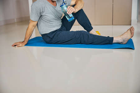 Sporty man with his water bottle sitting on a mat