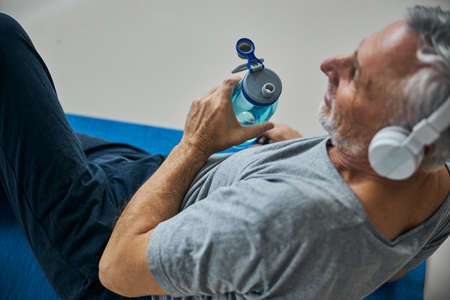 Positive elderly man with a water bottle listening to musicの写真素材