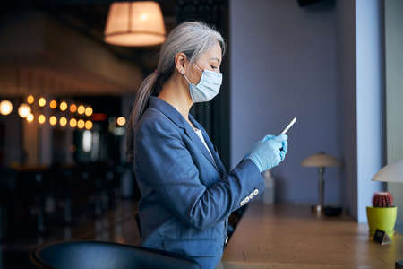 Businesswoman in medical mask using modern smartphoneの写真素材