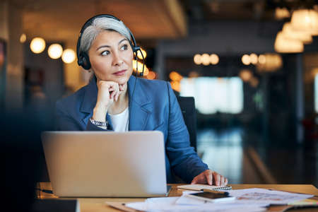 Beautiful woman in headphones sitting at the table with laptopの写真素材