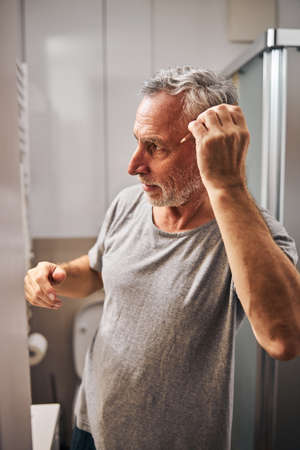 Serious eldelry man fixing his hair with a combの写真素材