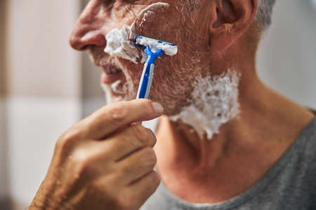 Gladsome aged man doing a shaving routineの写真素材