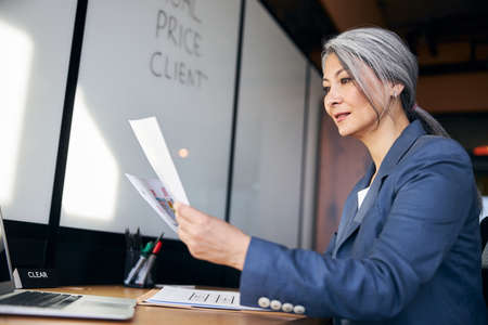 Beautiful woman studying architectural plans and using laptop at workの写真素材