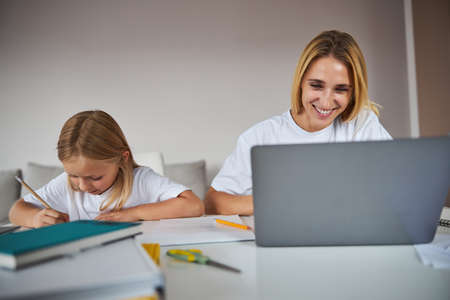 Business woman doing work tasks on a laptop while little girl sitting near her at the book