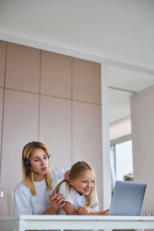 Happy smiling little girl and woman sitting at the desk while surfing internet in apartmentの写真素材