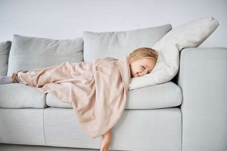 Happy smiling little miss relaxing on cozy grey sofa in living roomの写真素材