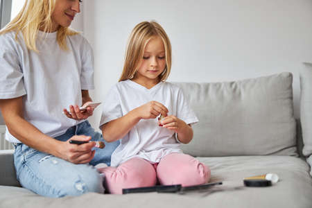 Seriously daughter with charming woman spending time together while sitting on the cozy sofa in living roomの写真素材