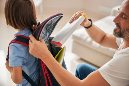 Helpful father packing books into rucksack on his son backの写真素材