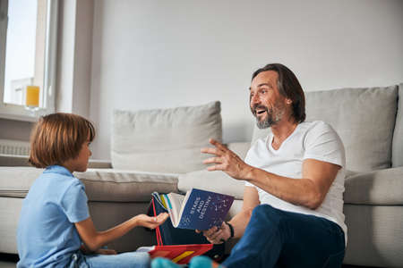 Joyful father holding a book while sitting with his son