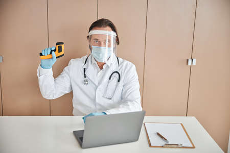 Professional medic with a thermometer in hand posing in office