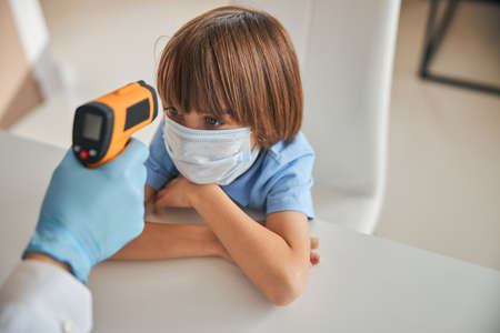 Diligent kid in a mask having his temperature takenの写真素材