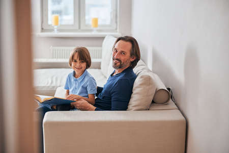 Adorable kid and his bearded dad resting on sofaの写真素材
