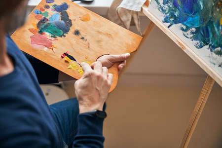 Dedicated artist mixing colors for painting on canvas