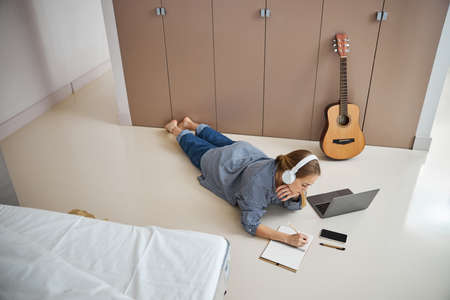 Charming female musician in headphones writing in spiral notebook