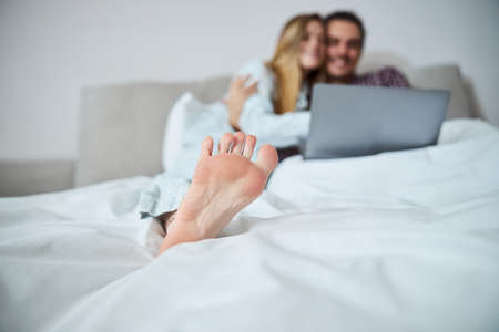 Barefoot young woman cuddling with boyfriend in bedの写真素材