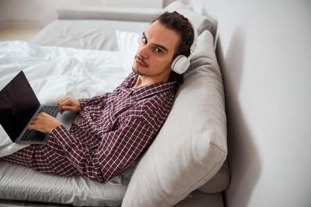 Good-looking young man in pajamas using laptop at homeの写真素材