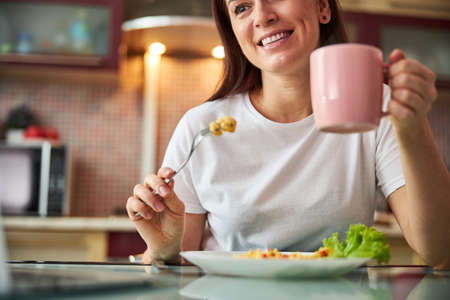 Housewife lifting a teacup while sitting over the meal