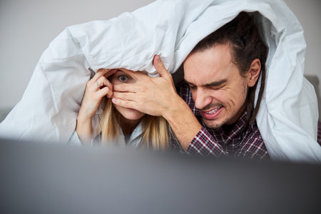 Beautiful young couple watching horror film on laptopの写真素材