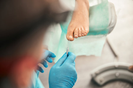 Attentive podologist doing medical pedicure for visitorの写真素材