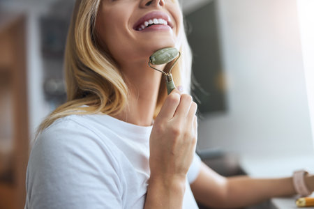 Focused image of blonde Caucasian female caring for neck with beauty toolの写真素材
