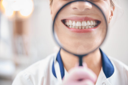 Joyful female dentist smiling through magnifier in officeの写真素材