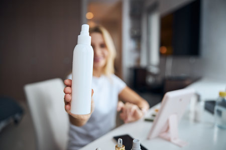 Elegant woman in white clothes demonstrating cosmetic container in room indoorsの写真素材