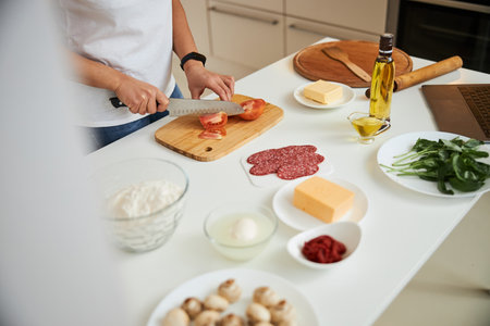 Slicing tomato while getting all the ingredients ready for the pizzaの写真素材
