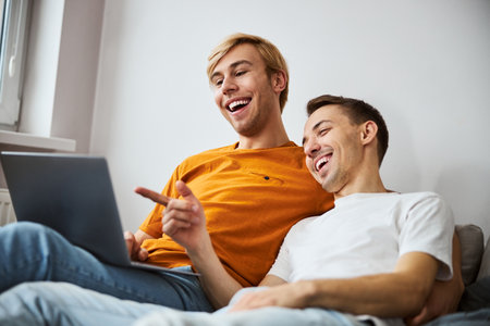 Happy gay couple watching movie on laptop at homeの写真素材