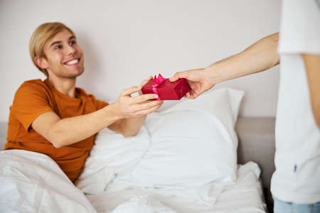 Cheerful young man accepting gift box from boyfriendの写真素材