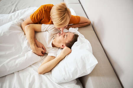 Happy homosexual couple touching noses and cuddling in bed