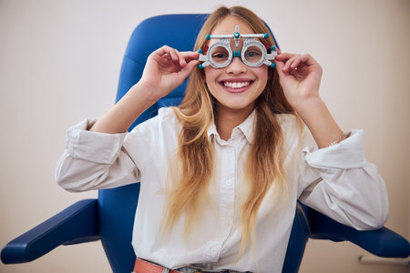 Happy smiling cute female child in casual clothes posing at the photo camera in modern optometrist cabinetの写真素材