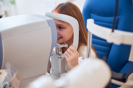 Happy smiling cute girl looking at slit lamp during medical check up in eyes clime in optometrist...