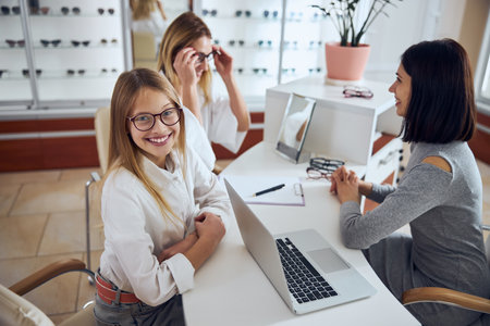 Beautiful funny teenager girl spending time with woman in ophthalmology clinicの写真素材