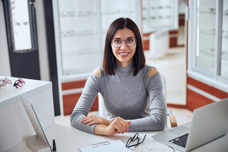 Beautiful Caucasian woman in grey clothes sitting at the work desk in room indoorsの写真素材