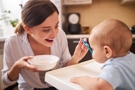 Positive delighted young parent feeding her babyの写真素材