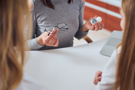 Woman seller demonstrating modern lens and eye glass in optician clinicの写真素材