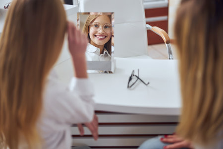 Happy smiling school girl wearing stylish eyeglasses in optician shopの写真素材