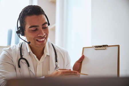 Positive male doctor in white robe showing white paper in cabinetの写真素材