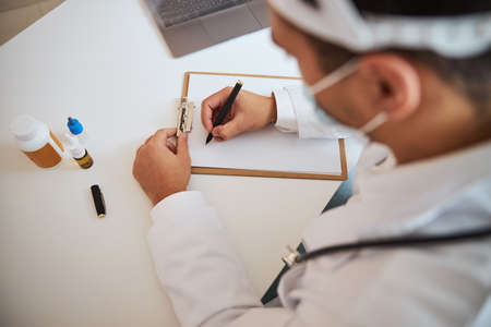 Focused image of confident male therapist doing notes on clipboard in room indoors of medical clinicの写真素材