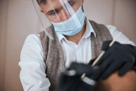 Seriously hair stylist in classic clothes working with visitor in barber shopの写真素材