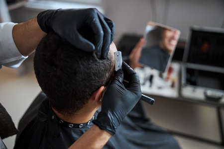Neat man in black peignoir getting hairdressing in beauty salon
