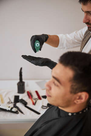 Bearded barber squeezing spray on arm while standing near the client in beauty salonの写真素材