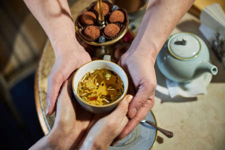 Two people joing their hands and holding cup of teaの写真素材