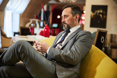 Concentrated businessman checking his phone updates art hotel lounge