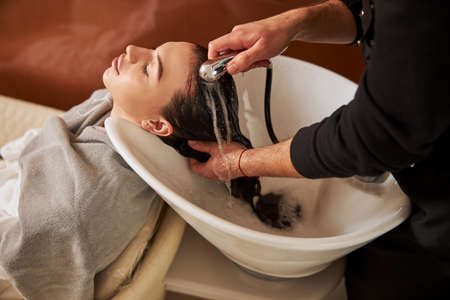 Male stylist rinsing the young client hairの写真素材
