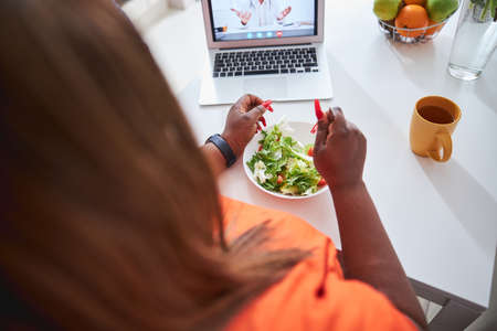 Brunette lady having salad while watching movie on laptopの写真素材