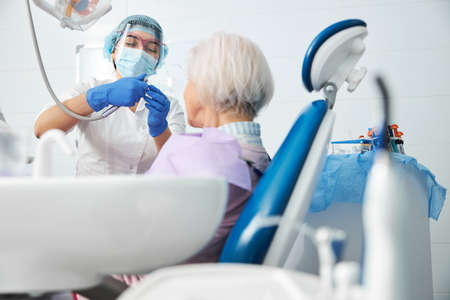Female dentist assembling a dental drill before aged womanの写真素材
